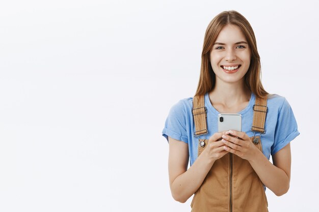 Sonriente chica atractiva que usa el teléfono móvil, envía mensajes de texto o navega por las redes sociales