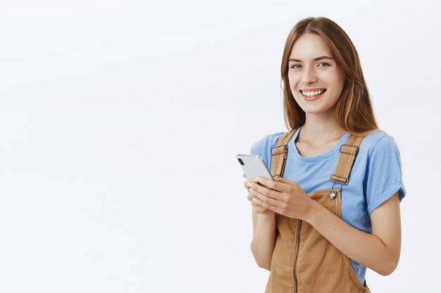 Sonriente chica atractiva que usa el teléfono móvil, envía mensajes de texto o navega por las redes sociales