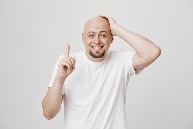 Sonriente chico calvo incómodo apuntando hacia arriba y riendo