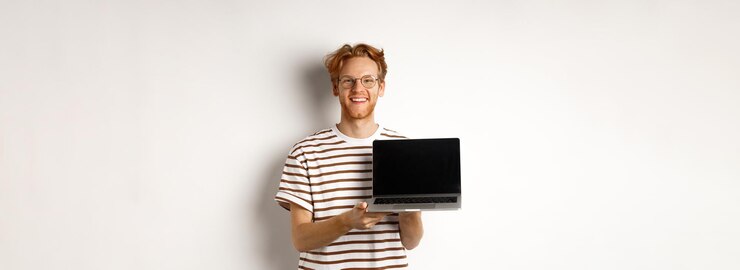 Foto gratuito sonriente chico pelirrojo orgulloso mostrando la pantalla de un portátil vacío apuesto joven demostrando el logotipo en compu