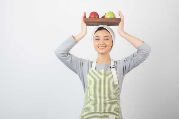 sonriente cocinera sosteniendo un plato de manzanas en blanco.