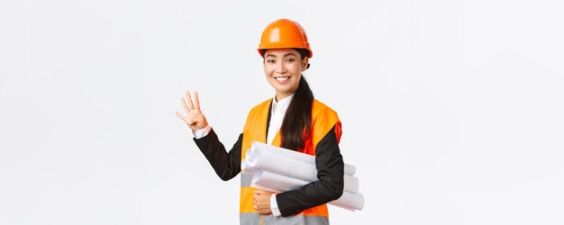 Sonriente confiada ingeniera asiática gerente de construcción en casco de seguridad llevar planos showi