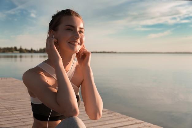 Sonriente dama de deportes en la playa escuchando música con auriculares