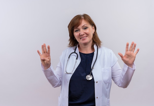 Sonriente doctora de mediana edad vistiendo bata médica y estetoscopio mostrando cuatro y cinco en una pared blanca aislada con espacio de copia