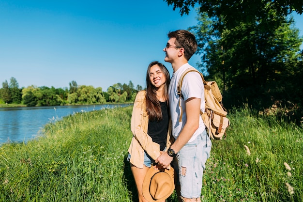 Sonriente encantadora joven pareja de pie en la hierba verde cerca del lago