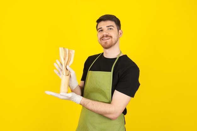 Sonriente a feliz joven sosteniendo utensilios de cocina y mirando a cámara.