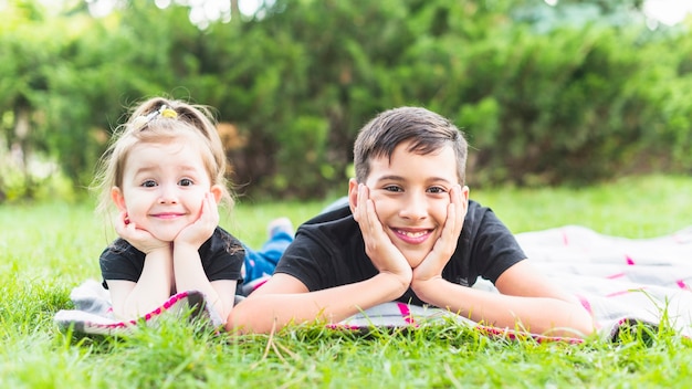 Sonriente hermano y hermana acostado sobre una manta sobre la hierba verde