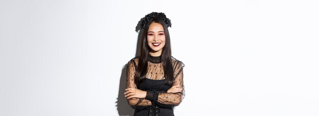 Sonriente hermosa mujer asiática celebrando halloween con corona negra y vestido de maquillaje gótico loo