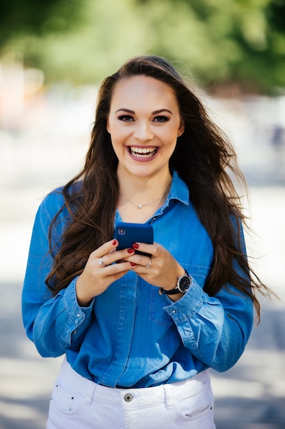 Sonriente hermosa mujer urbana con teléfonos inteligentes en la calle