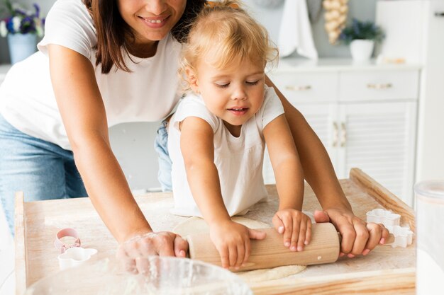 Sonriente hija y madre con rodillo de cocina