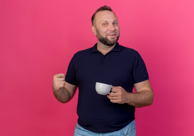 Sonriente hombre adulto eslavo sosteniendo la taza y apuntando aislado