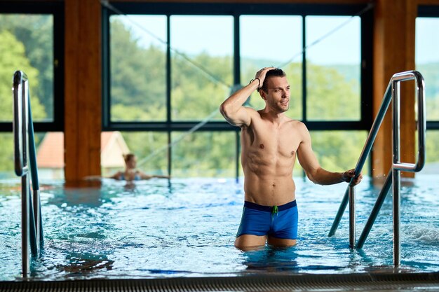 Sonriente hombre adulto medio saliendo de la piscina en el spa y mirando hacia otro lado Copiar espacio