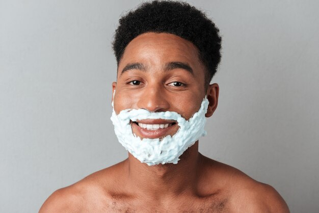 Sonriente hombre africano desnudo con cara en espuma de afeitar