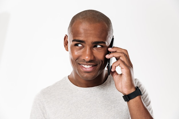 Sonriente hombre africano hablando por el teléfono inteligente y mirando a otro lado