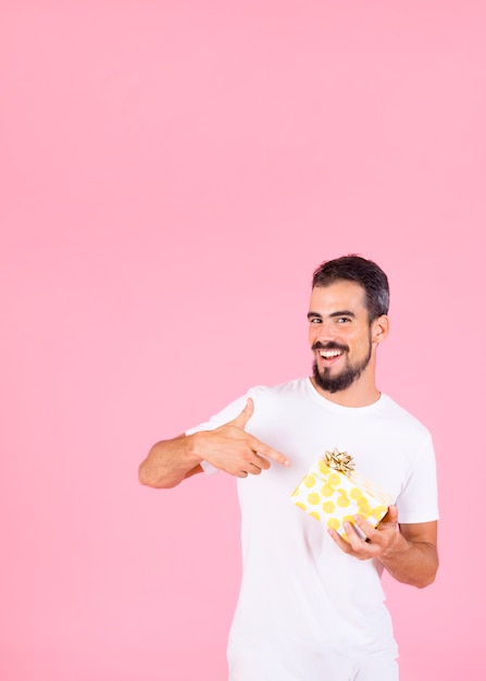 Sonriente hombre apuntando dedo mostrando caja de regalo con lazo dorado