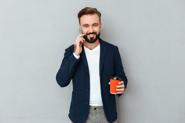 Sonriente hombre barbudo en ropa de negocios hablando por teléfono inteligente