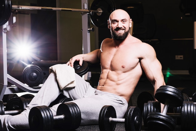 Sonriente hombre barbudo sentado en medio de pesas