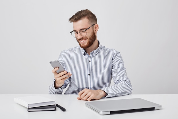 Sonriente hombre elegante beraded tiene una expresión feliz mientras recibe un mensaje agradable