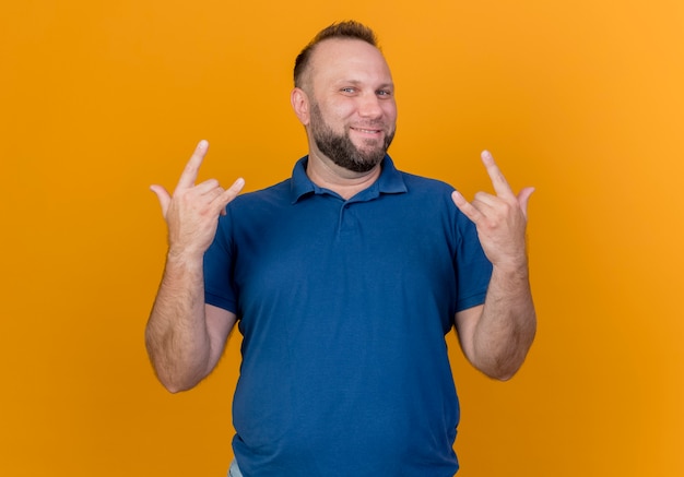 Sonriente hombre eslavo adulto haciendo signos de rock aislados en la pared naranja