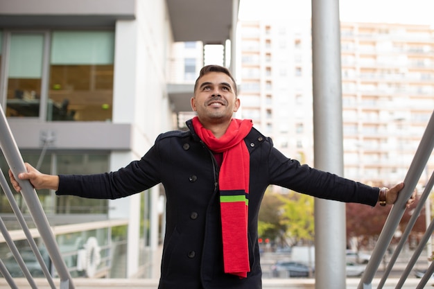 Foto gratuita sonriente hombre guapo en abrigo y bufanda roja subiendo escaleras