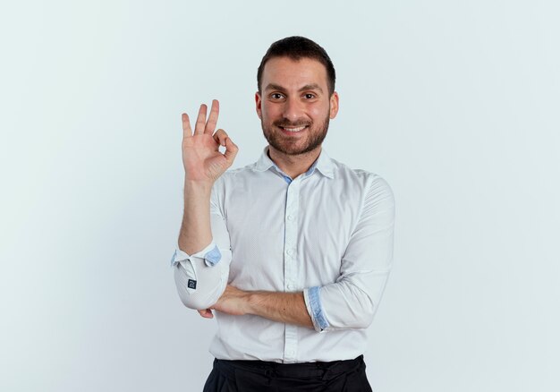 Sonriente hombre guapo gestos ok signo de mano mirando aislado en la pared blanca