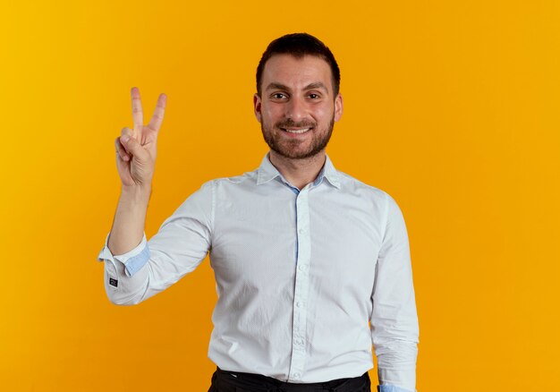 Sonriente hombre guapo gestos victoria signo de mano aislado en la pared naranja