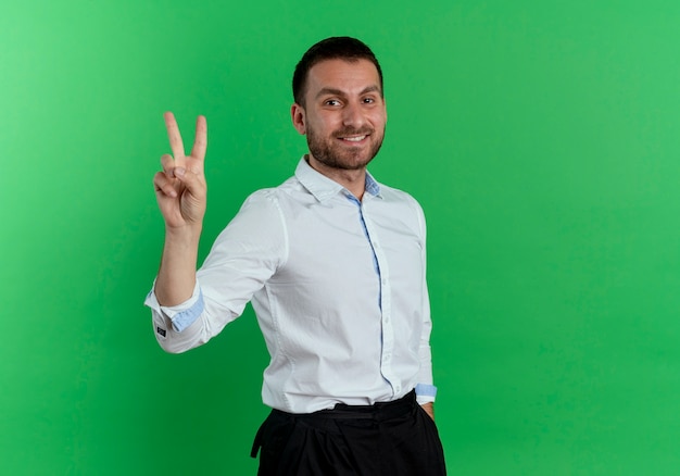 Sonriente hombre guapo gestos victoria signo de mano aislado en la pared verde