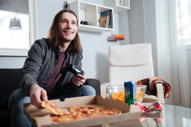 Sonriente hombre jugador sentado en su casa en el interior y jugar juegos