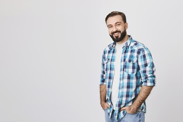 Sonriente hombre de mediana edad con barba de pie sobre fondo gris