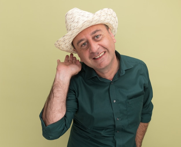 Sonriente hombre de mediana edad vestido con camiseta verde y puntos de sombrero detrás aislado en la pared verde oliva con espacio de copia