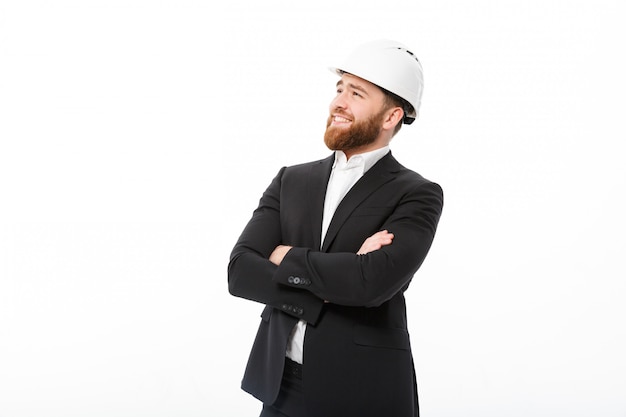 Foto gratuita sonriente hombre de negocios barbudo en casco protector con brazos cruzados