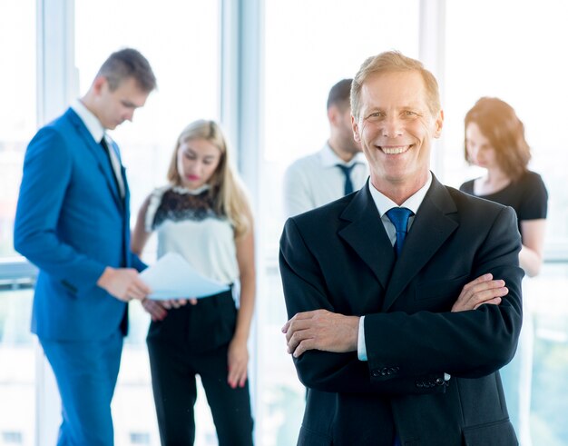 Sonriente hombre de negocios maduro de pie delante de sus colegas en el lugar de trabajo