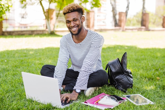 Sonriente hombre negro posando con la computadora portátil