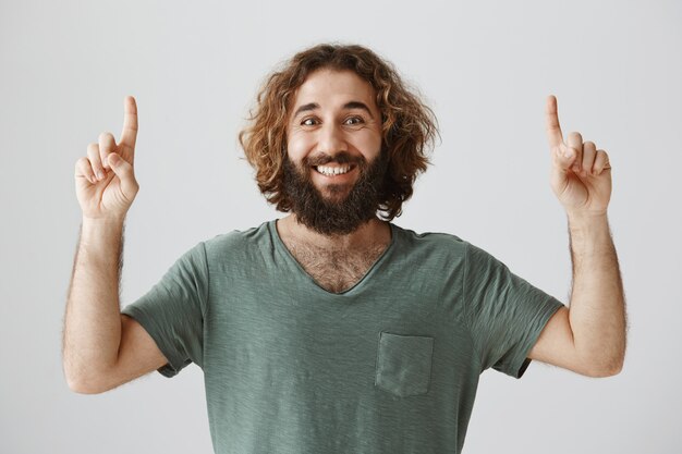 Sonriente hombre de Oriente Medio barbudo apuntando con el dedo hacia arriba