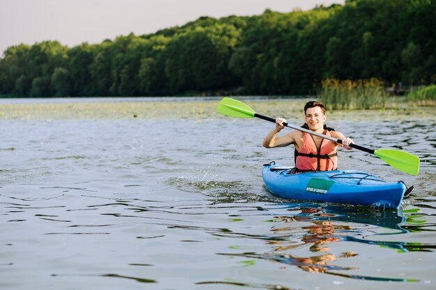 Sonriente hombre salpicaduras de agua mientras rema el kayak en el lago