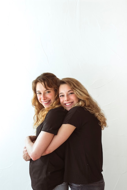 Foto gratuita sonriente joven abrazando a su hermana por detrás en el fondo blanco