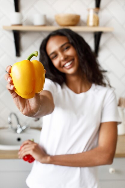 Sonriente joven afro muestra de cerca un pimiento amarillo