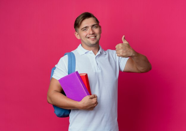 Sonriente joven apuesto estudiante vistiendo bolsa trasera sosteniendo libros