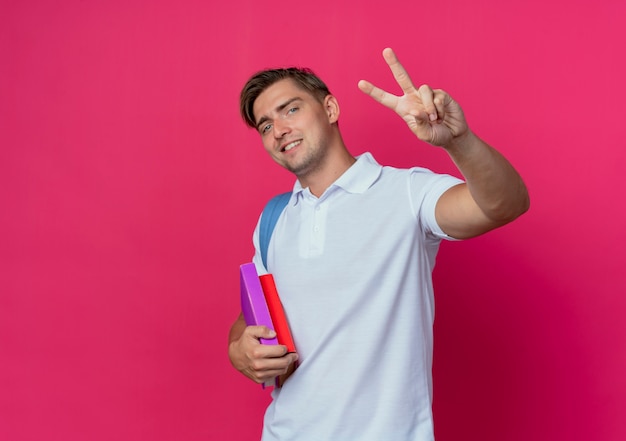 Foto gratuita sonriente joven apuesto estudiante vistiendo bolsa trasera sosteniendo libros