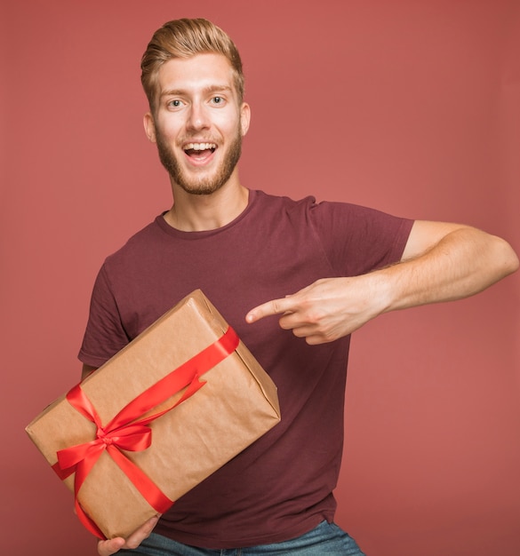 Sonriente joven apuntando el dedo hacia la caja de regalo envuelto