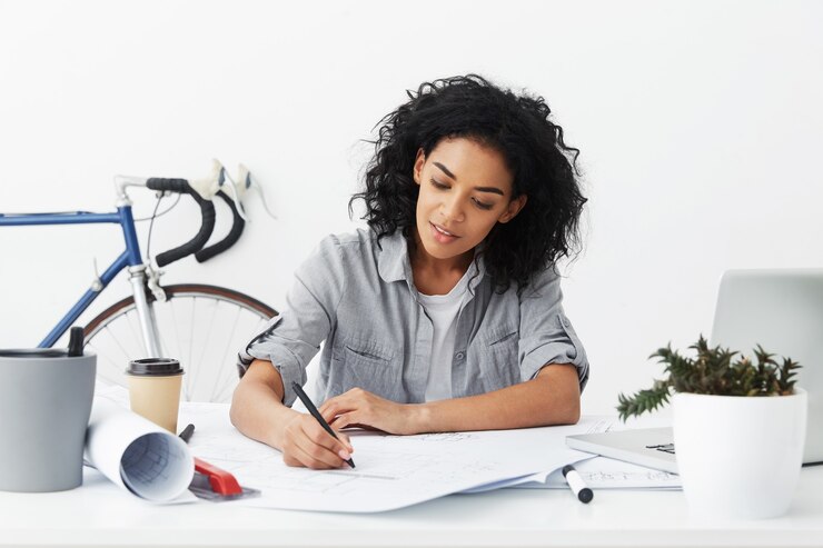 Foto gratuito sonriente joven arquitecto mujer autónoma de piel oscura con peinado afro haciendo dibujo