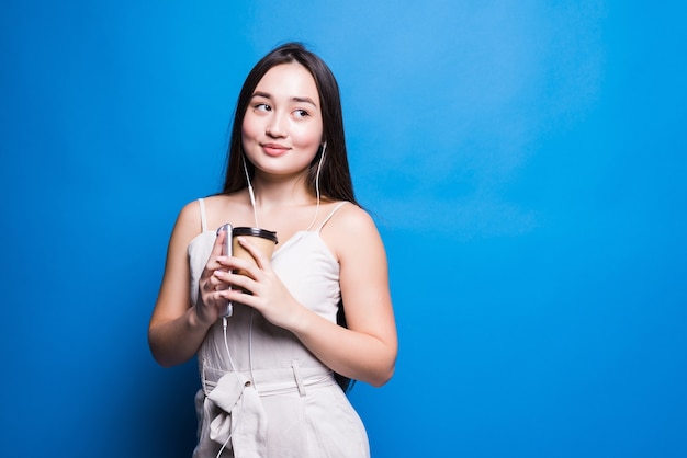 Sonriente joven asiática sosteniendo la taza de café para llevar que se encuentran aisladas sobre la pared azul