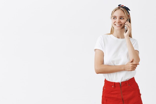 Sonriente joven atractiva rubia posando contra la pared blanca