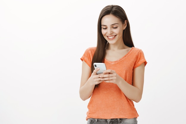 Foto gratuita sonriente joven atractiva mediante teléfono móvil