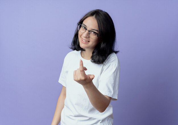 Sonriente joven bastante caucásica con gafas haciendo ven aquí gesto aislado sobre fondo púrpura con espacio de copia