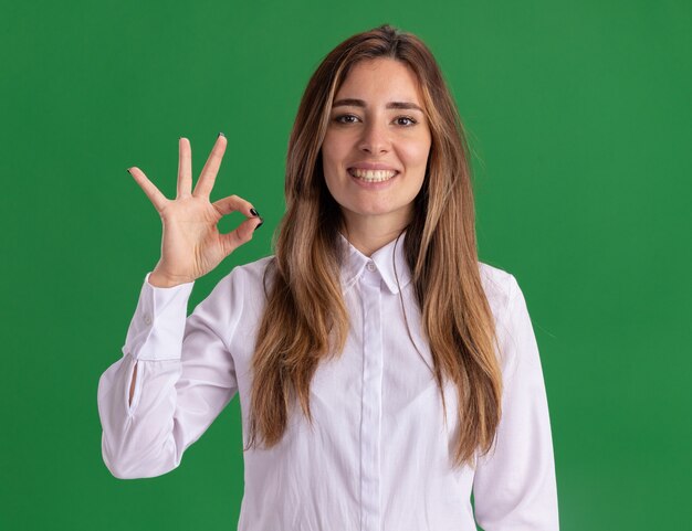 Sonriente joven bastante caucásica gestos ok mano firme en verde