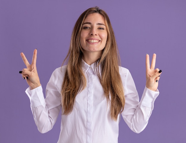 Foto gratuita sonriente joven bastante caucásica gestos signo de victoria con las dos manos en púrpura