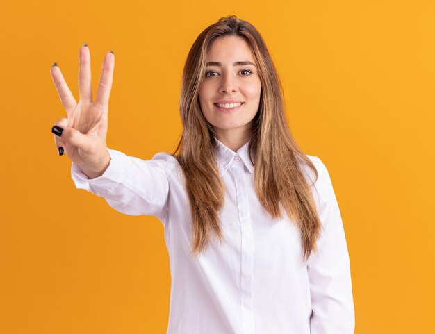 Sonriente joven bastante caucásica gestos tres con los dedos en naranja