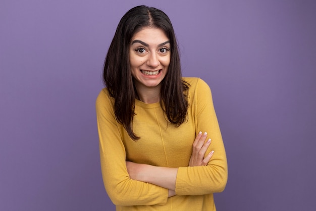 Sonriente joven bastante caucásica de pie con postura cerrada aislado en la pared púrpura con espacio de copia