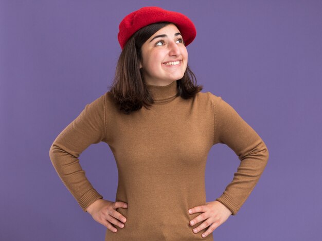 Sonriente joven bastante caucásica con sombrero de boina mirando al lado